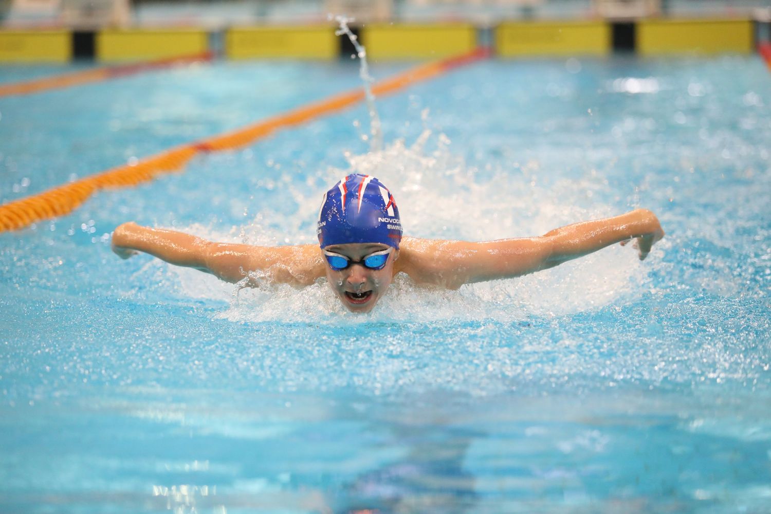 Swimmer executing butterfly stroke in competition pool with perfect form.