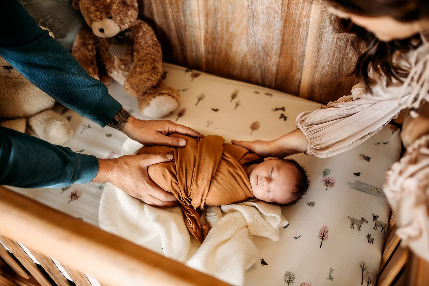 A mother and father lay their hands gently on their newborn boy while he sleeps in his crib.