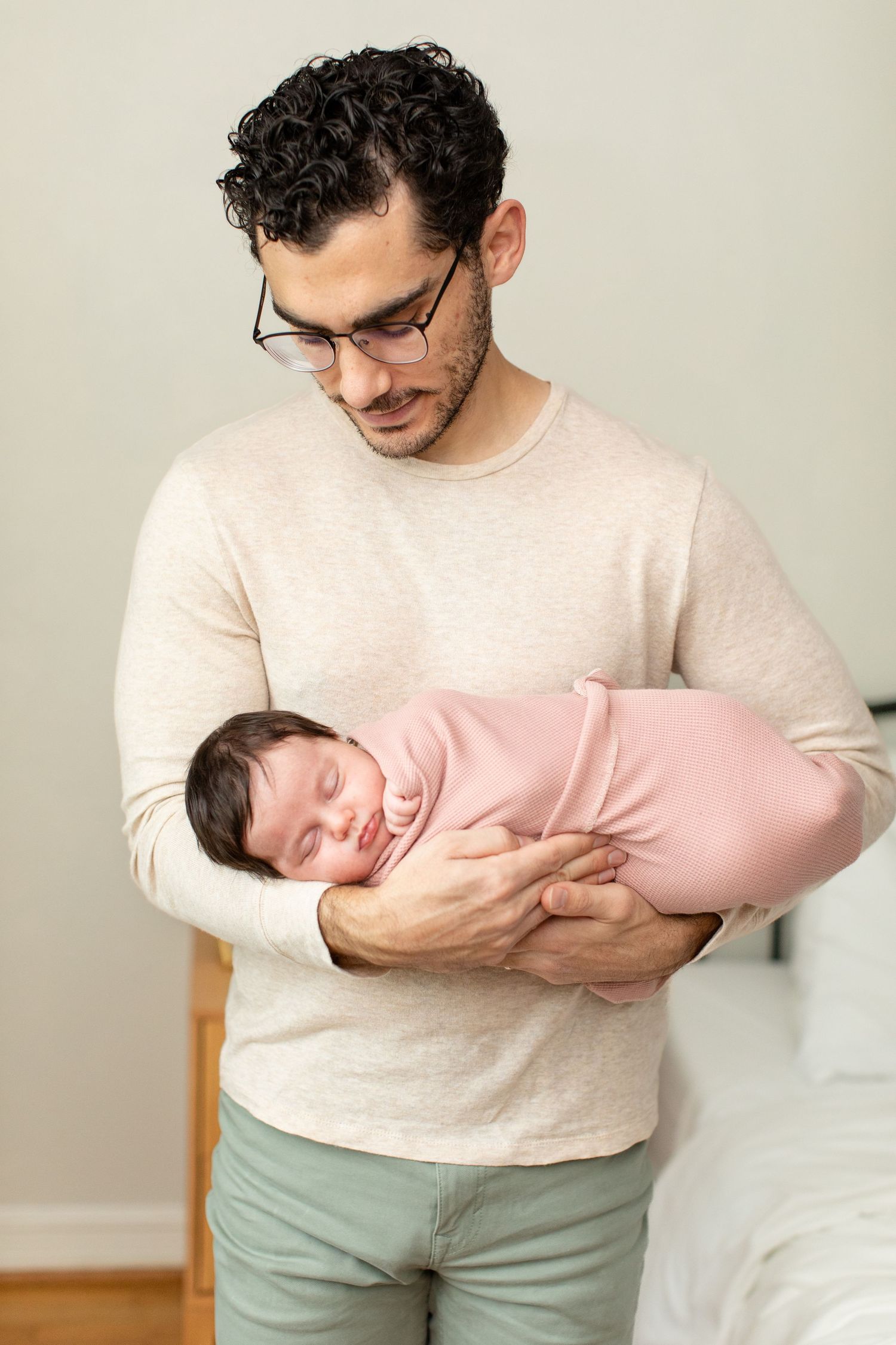 Parent in beige sweater gently holds sleeping newborn wrapped in pink swaddle.