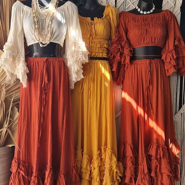 Collection of vintage-style dresses in rust, yellow and white tones hanging on wooden hangers.