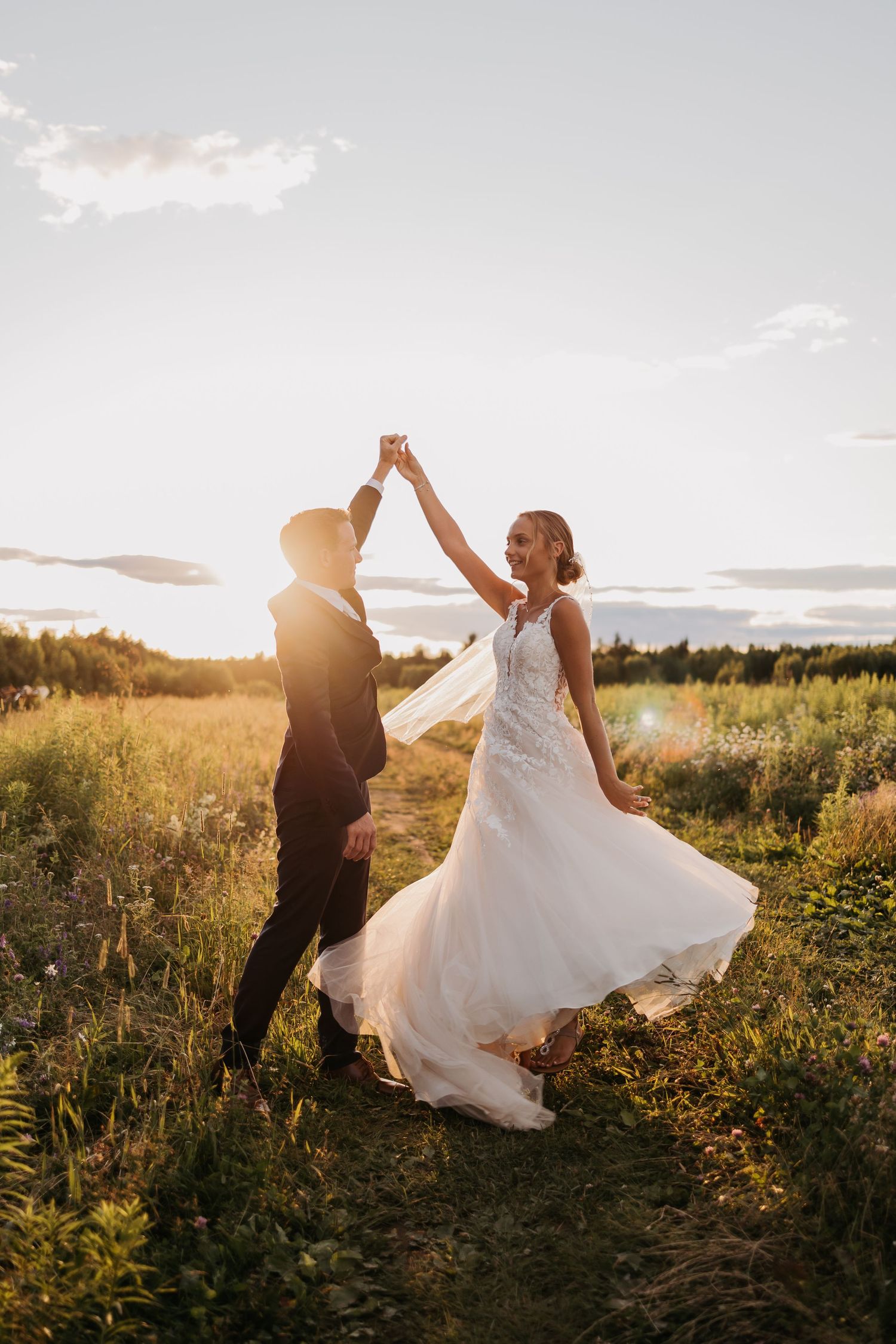 A couple dancing and twirling in a field during golden hour sunset.