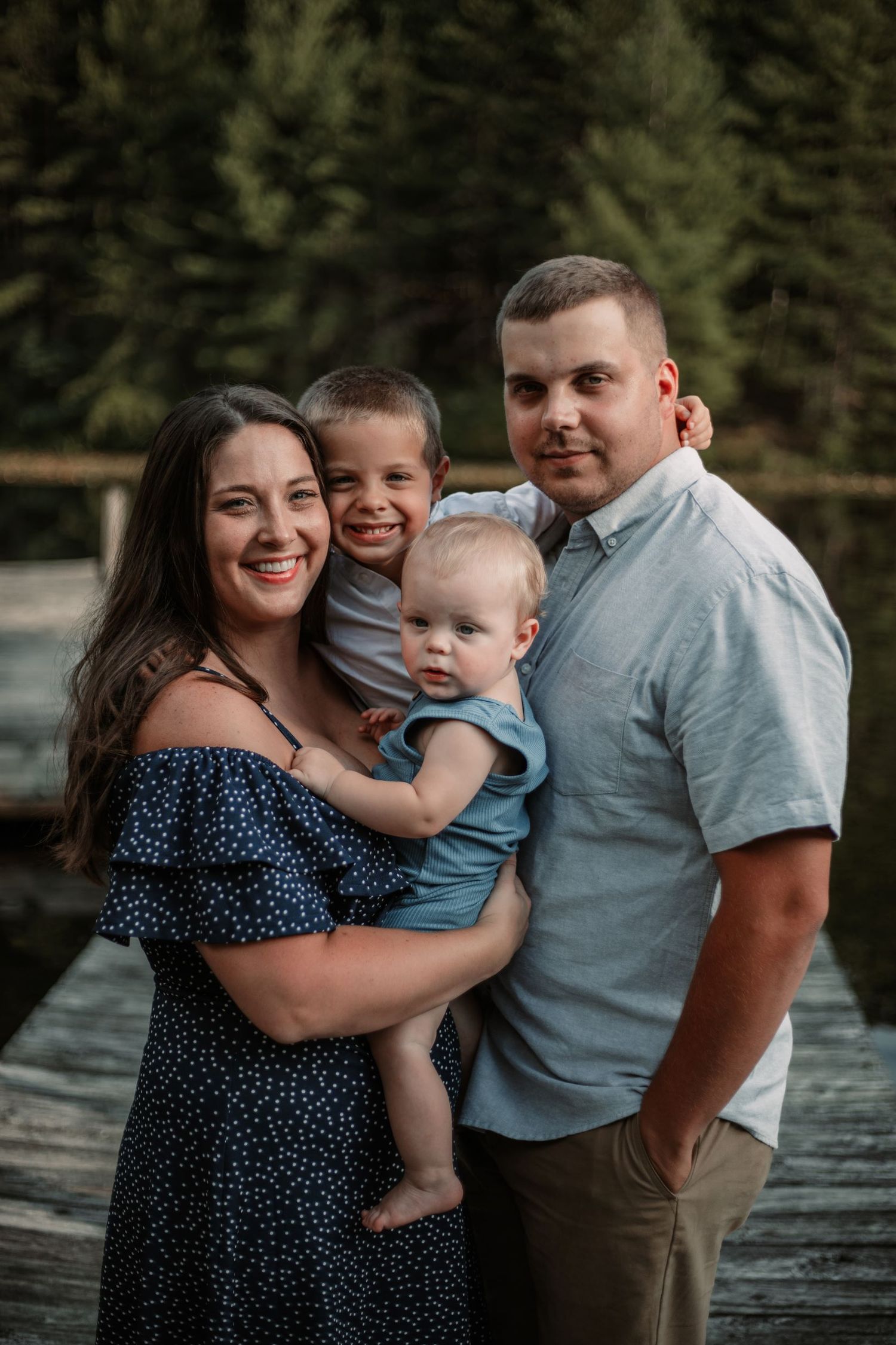 Family portrait on wooden dock with evergreen forest backdrop.