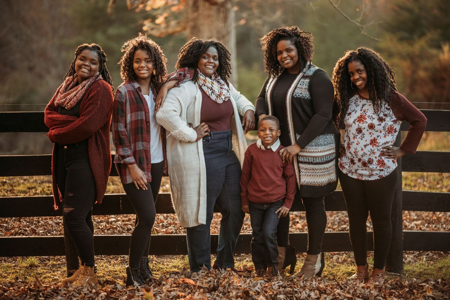 A group stands together outdoors on fallen autumn leaves wearing casual clothing in warm earth tones.