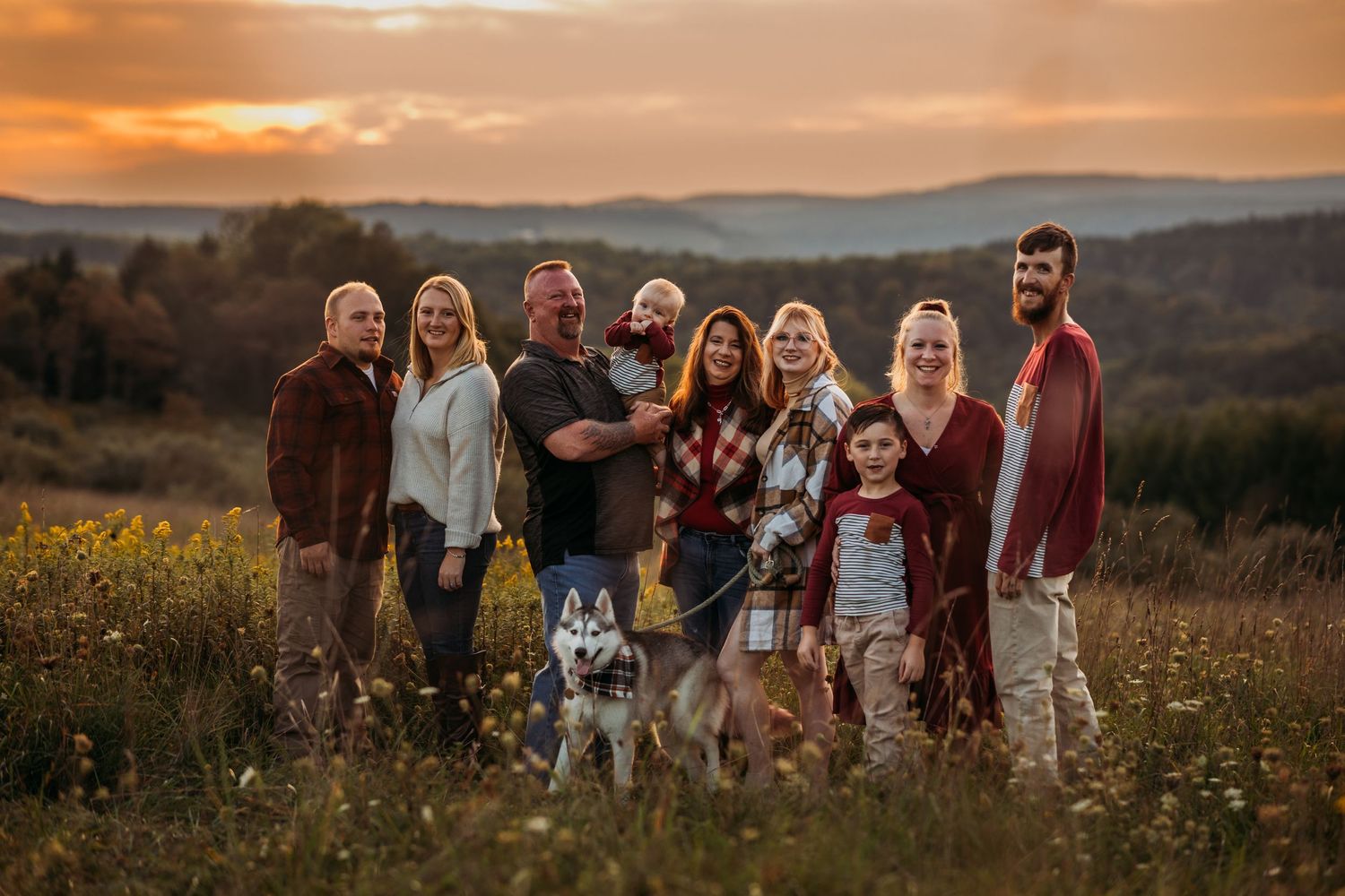 Large family group poses together with their dog in a field during golden sunset hour.