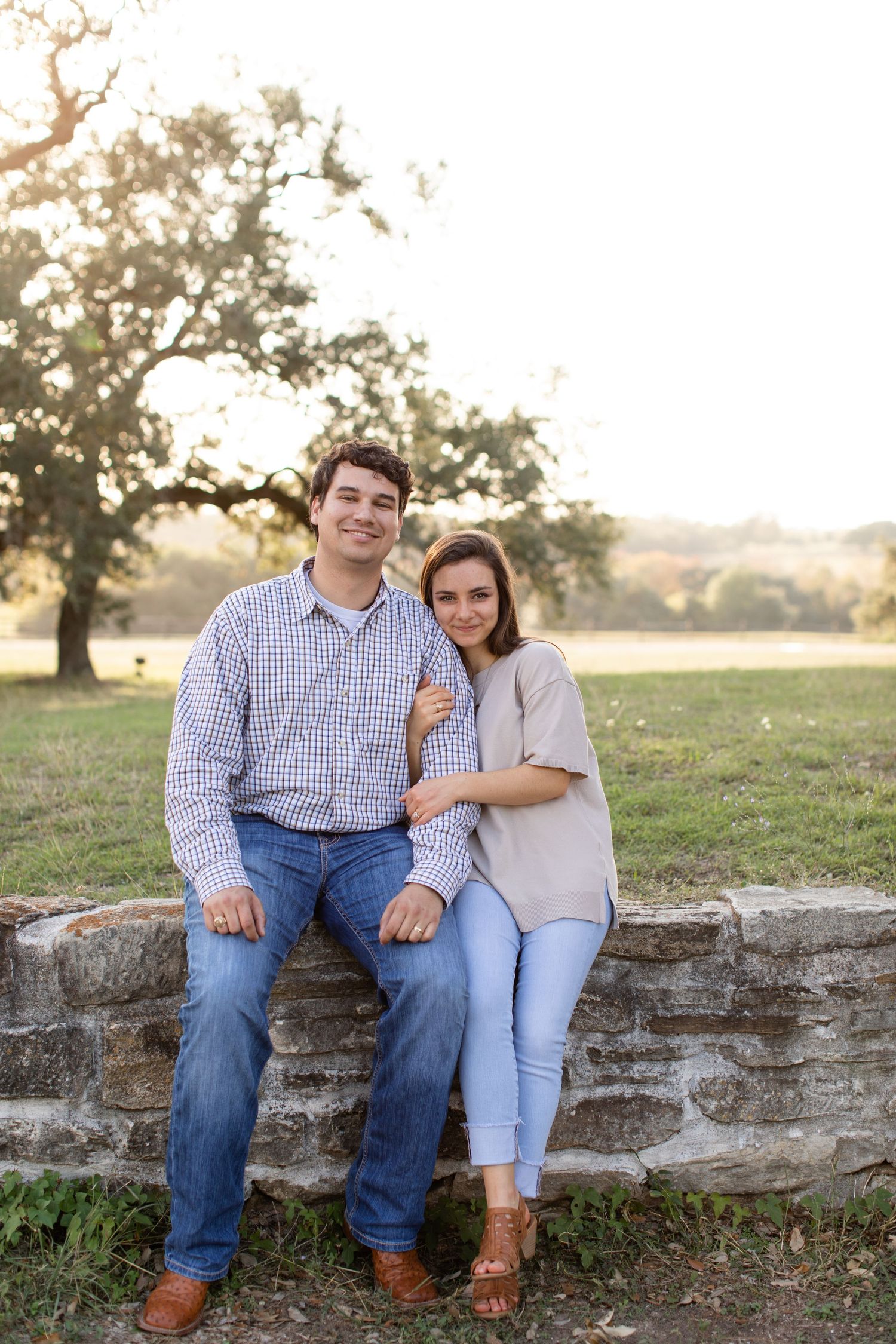 A couple sits together on an old stone wall during golden hour.