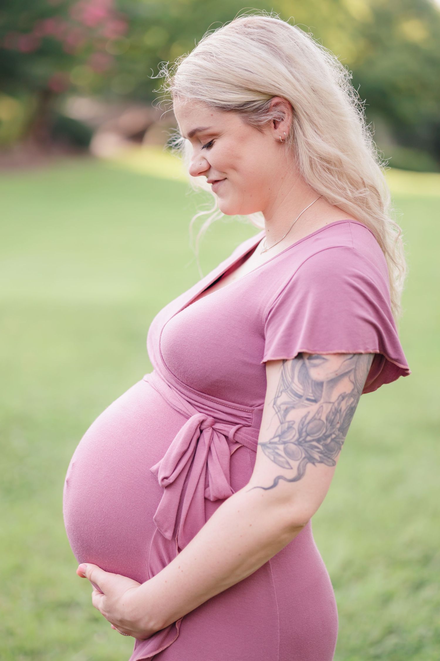 An expectant mother in a pink dress cradles her baby bump in a garden setting.