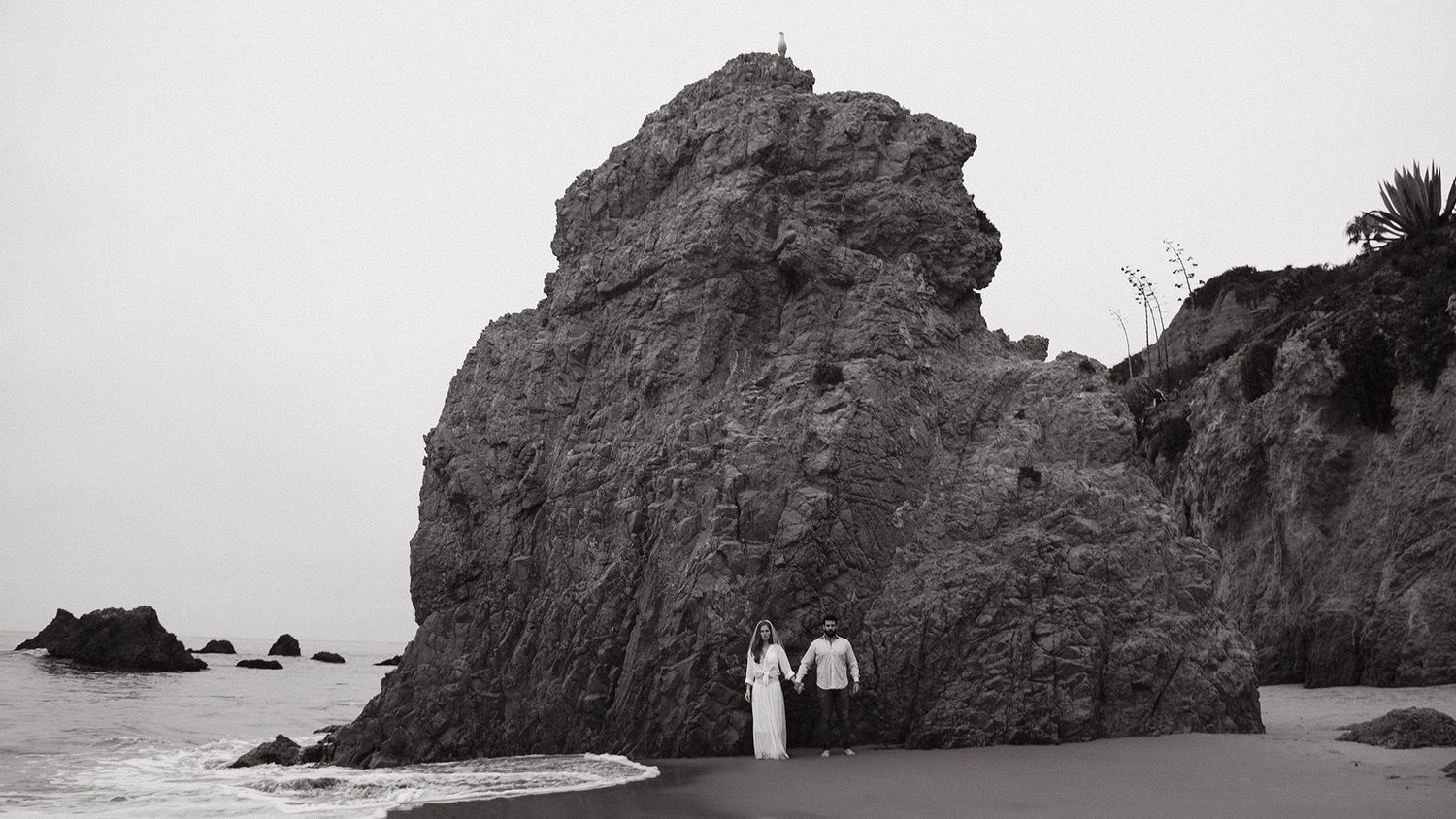 Black and white photograph of coastal rock formation with tiny figures for scale.