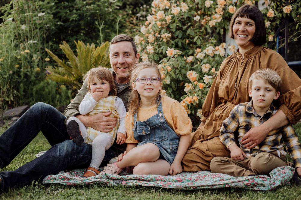 Family portrait on blanket with blooming roses and garden setting in background.