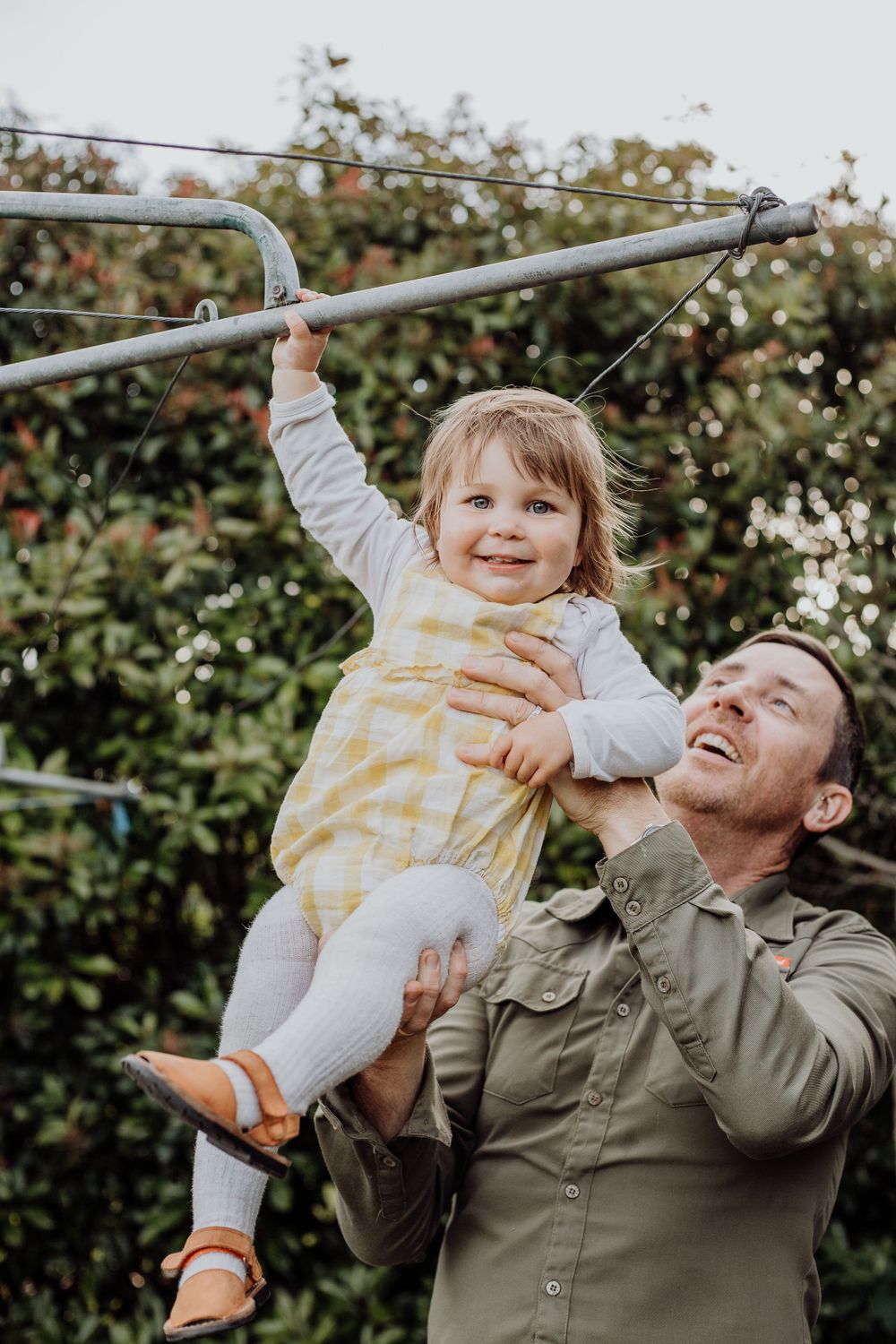 Playful moment at garden clothesline as toddler hangs while being supported.