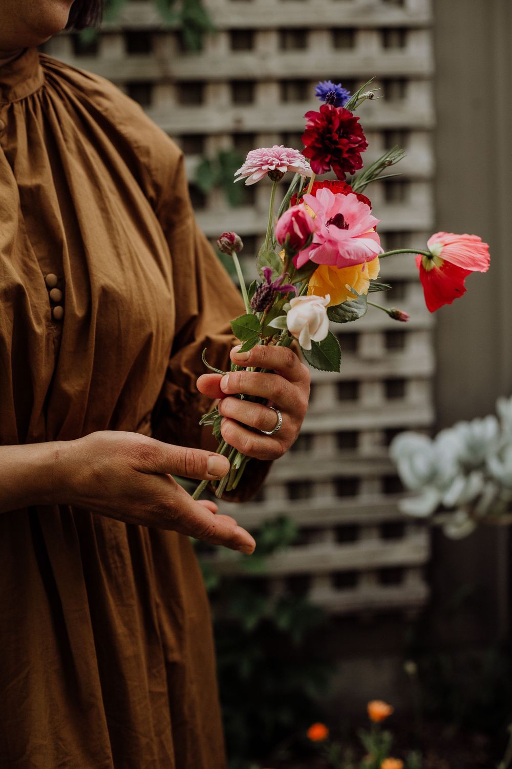Hands holding a delicate bouquet of colorful flowers including pink, red and purple blooms against a brown dress.