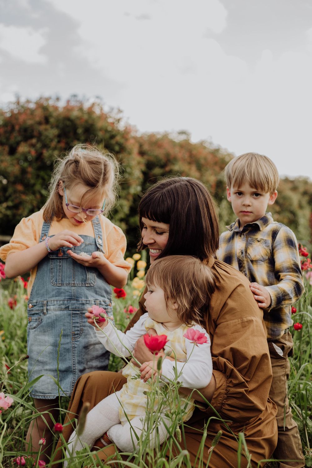 A family gathers together in a flower field picking and examining colorful blooms.