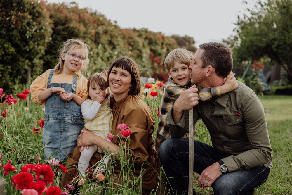 A family poses together among red flowers in a garden on a sunny afternoon.