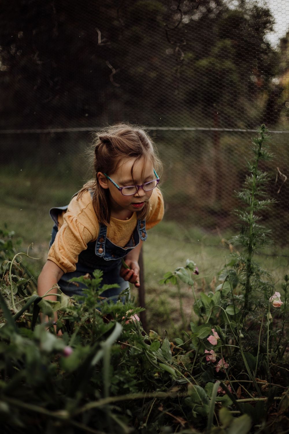 Young gardener in overalls and glasses tending to plants in a garden.