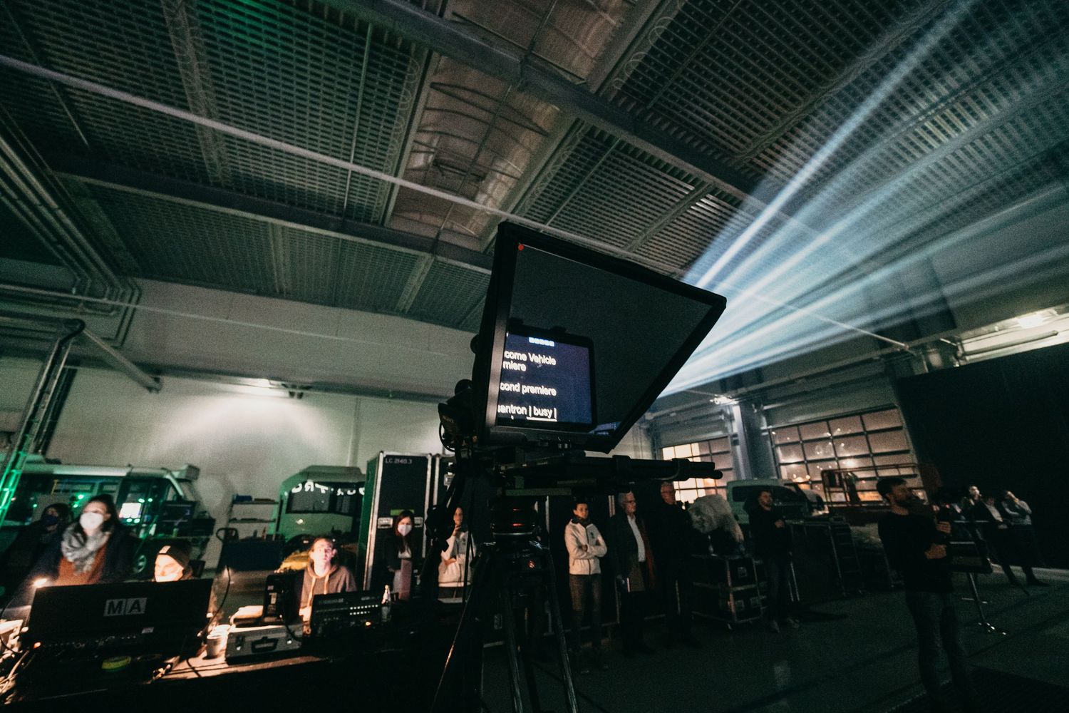 Ein Teleprompter mit englischem Text. Leute der Produktion stehen im Hintergrund