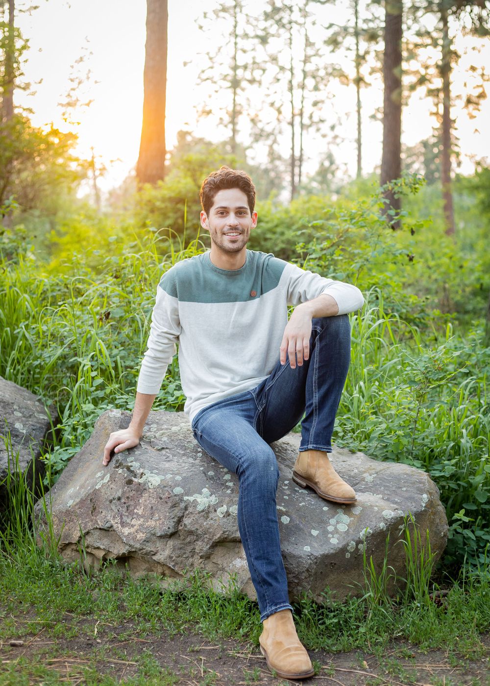 Casual portrait sitting on a rock during sunset in a wooded area.