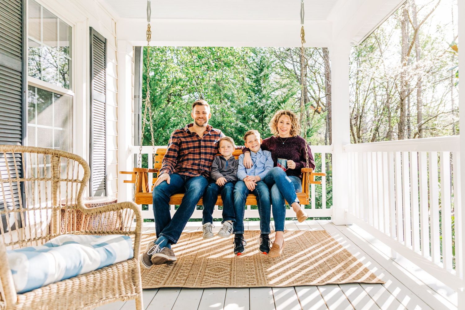Family of four sitting and smiling on their front porch swing