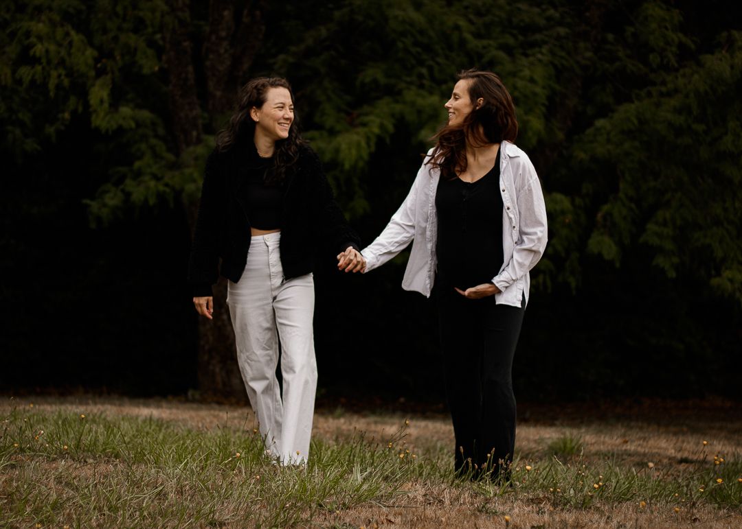 Two people walk hand-in-hand on a grassy path, surrounded by trees, enjoying a peaceful moment in nature together.