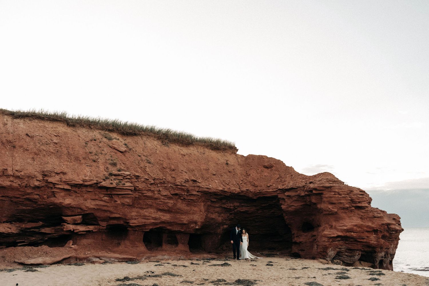Distant wedding couple silhouetted in natural rock arch formation.