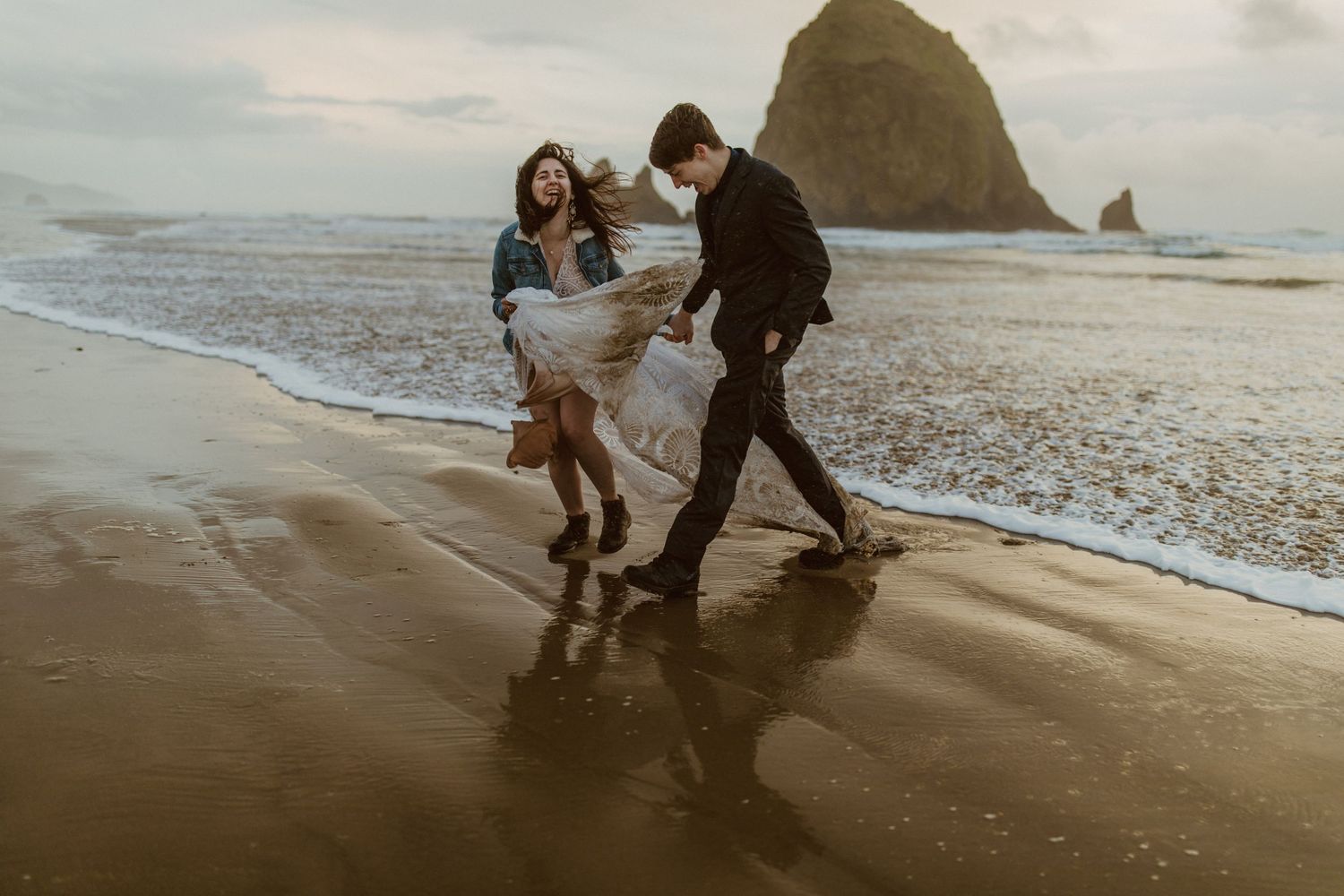 Couple walking along a misty beach shoreline at sunset with waves gently rolling in.