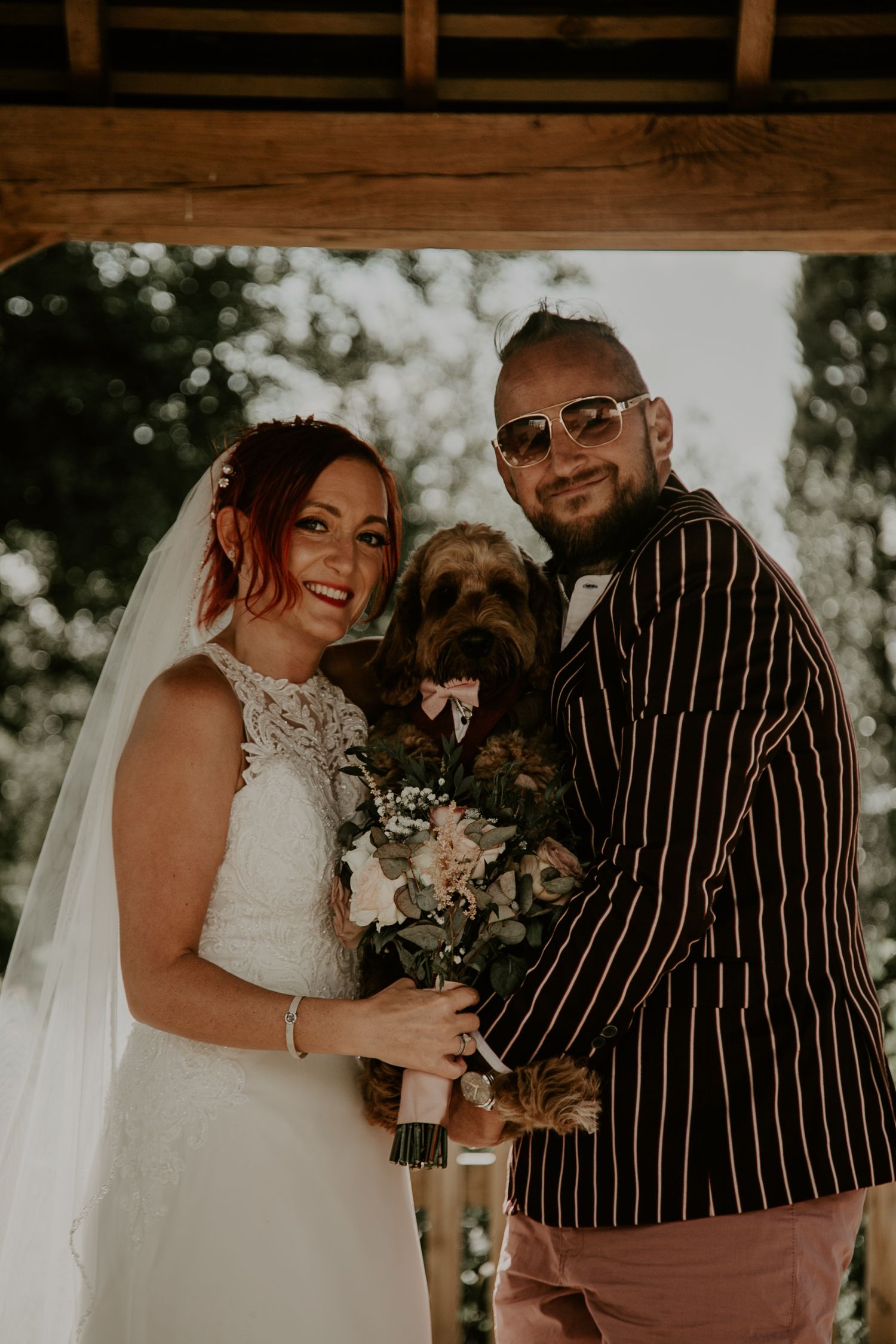 Couple in wedding attire embraces outdoors with striped suit and white dress details.