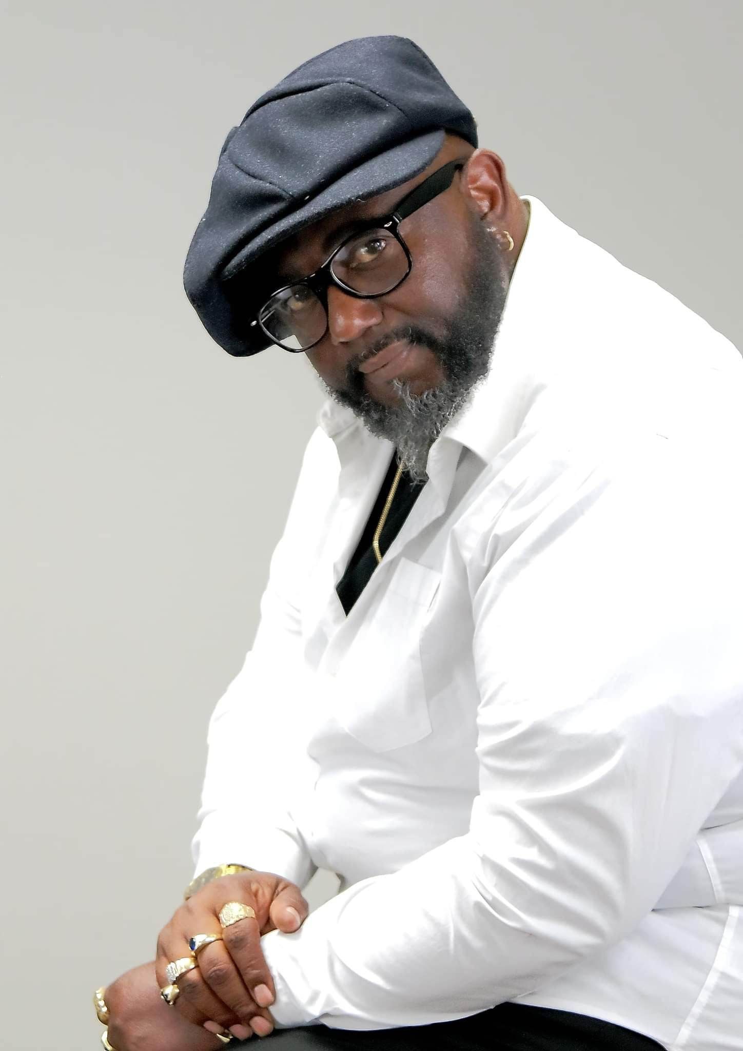 Professional studio portrait with newsboy cap and white shirt against grey background.