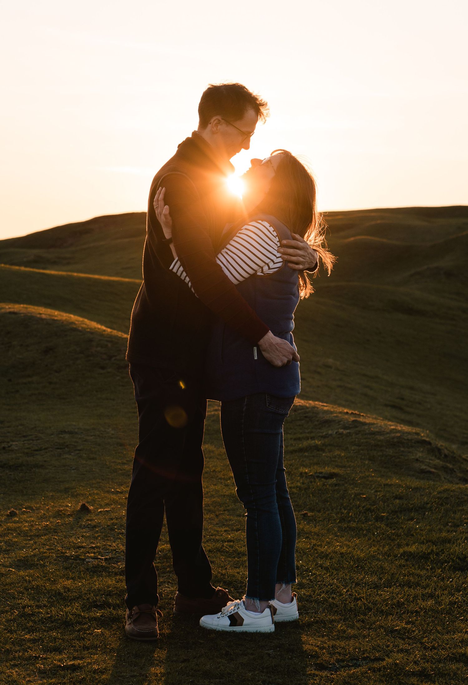 A young couple having a hug, looking at each other and the sun shining through the gap between their heads, at golden hour.