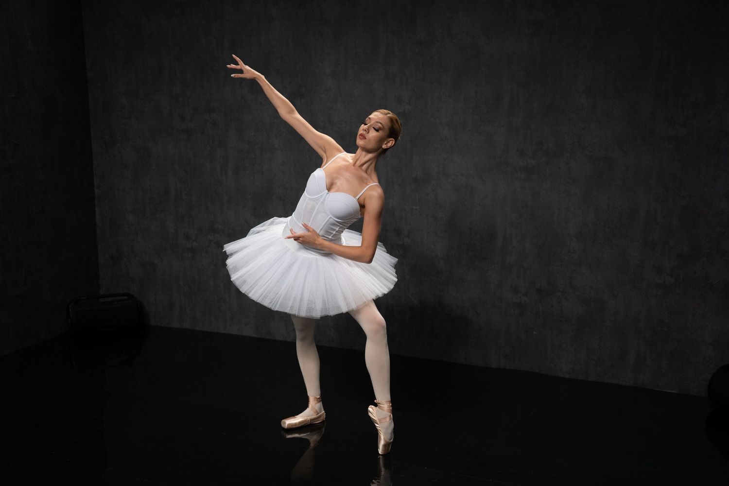 Ballet performer in white costume creates dramatic shapes against black background.