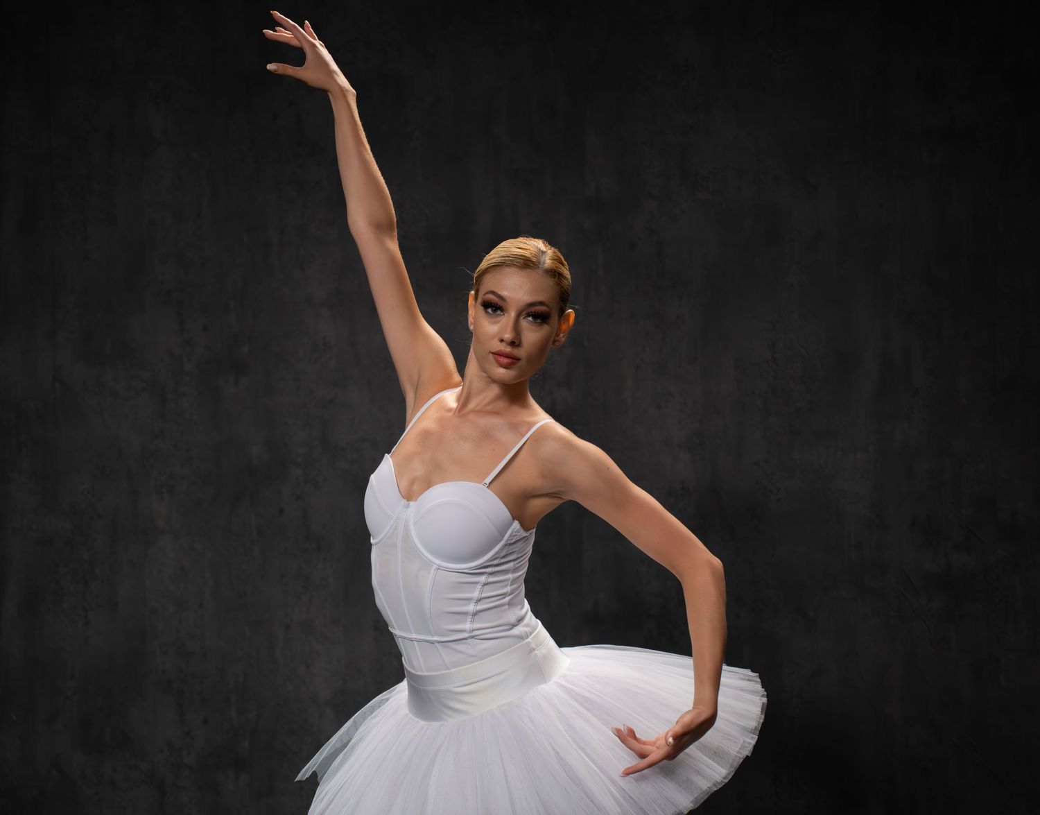 Ballerina in white tutu strikes elegant pose during studio performance.