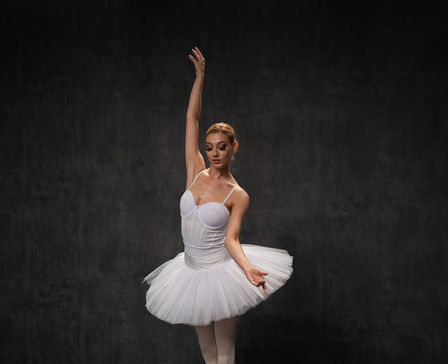 Dancer in traditional white tutu executes precise ballet movements in studio.