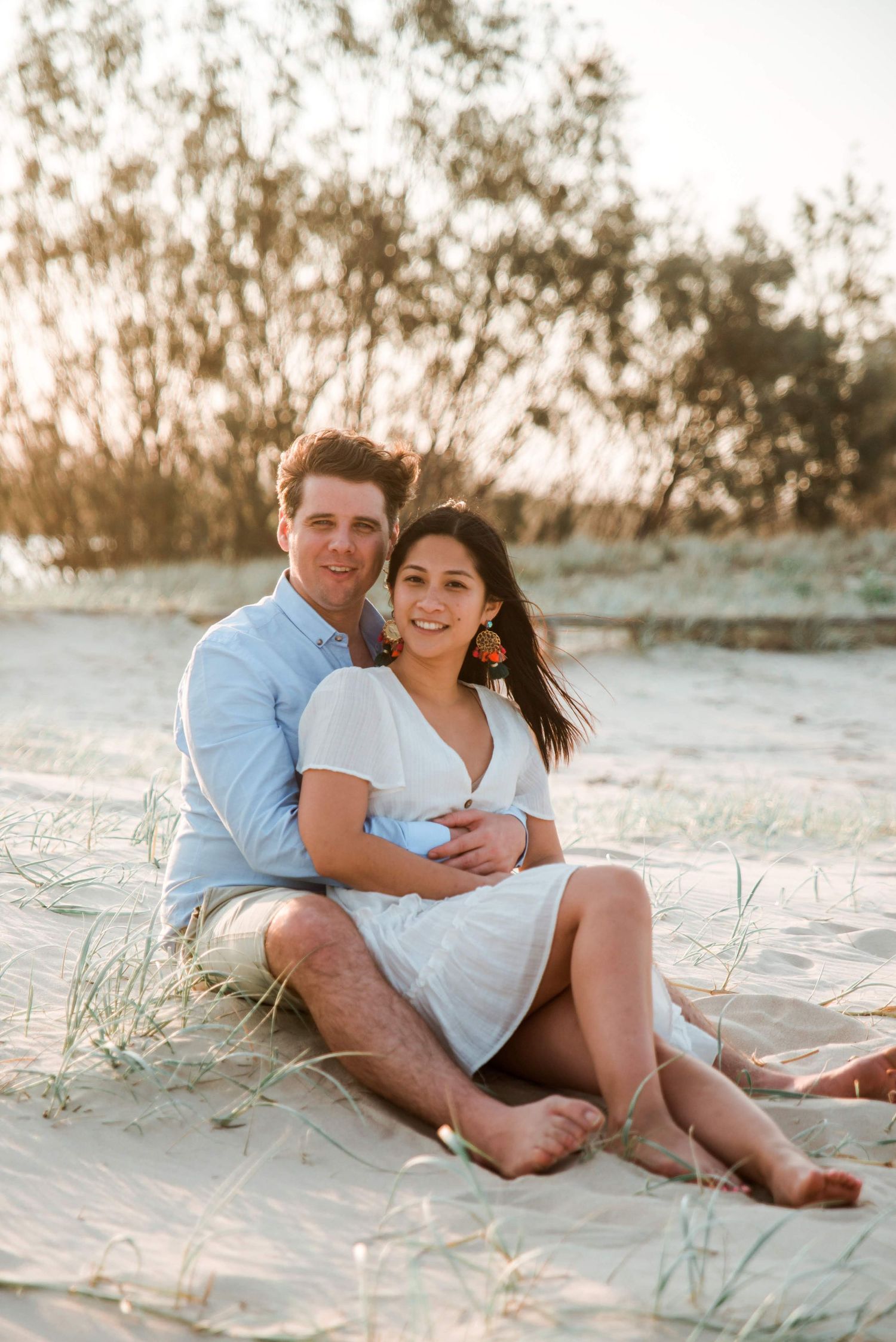 Romantic couple sitting together on sandy beach during golden hour sunset.