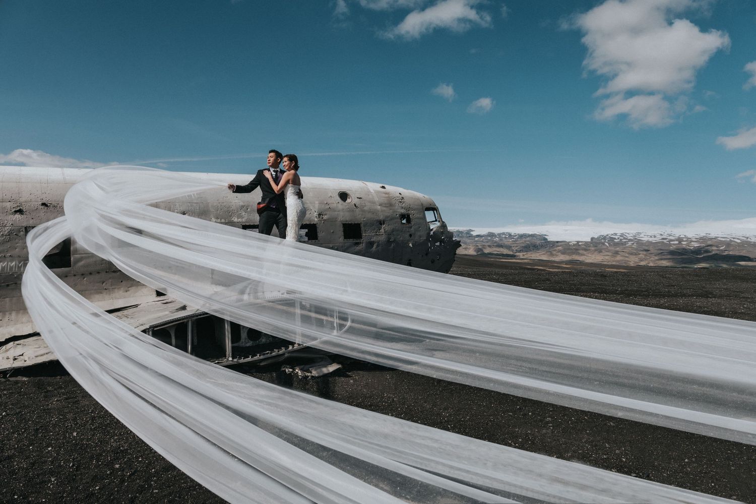 Wedding photo with flowing white dress against dramatic mountain landscape.