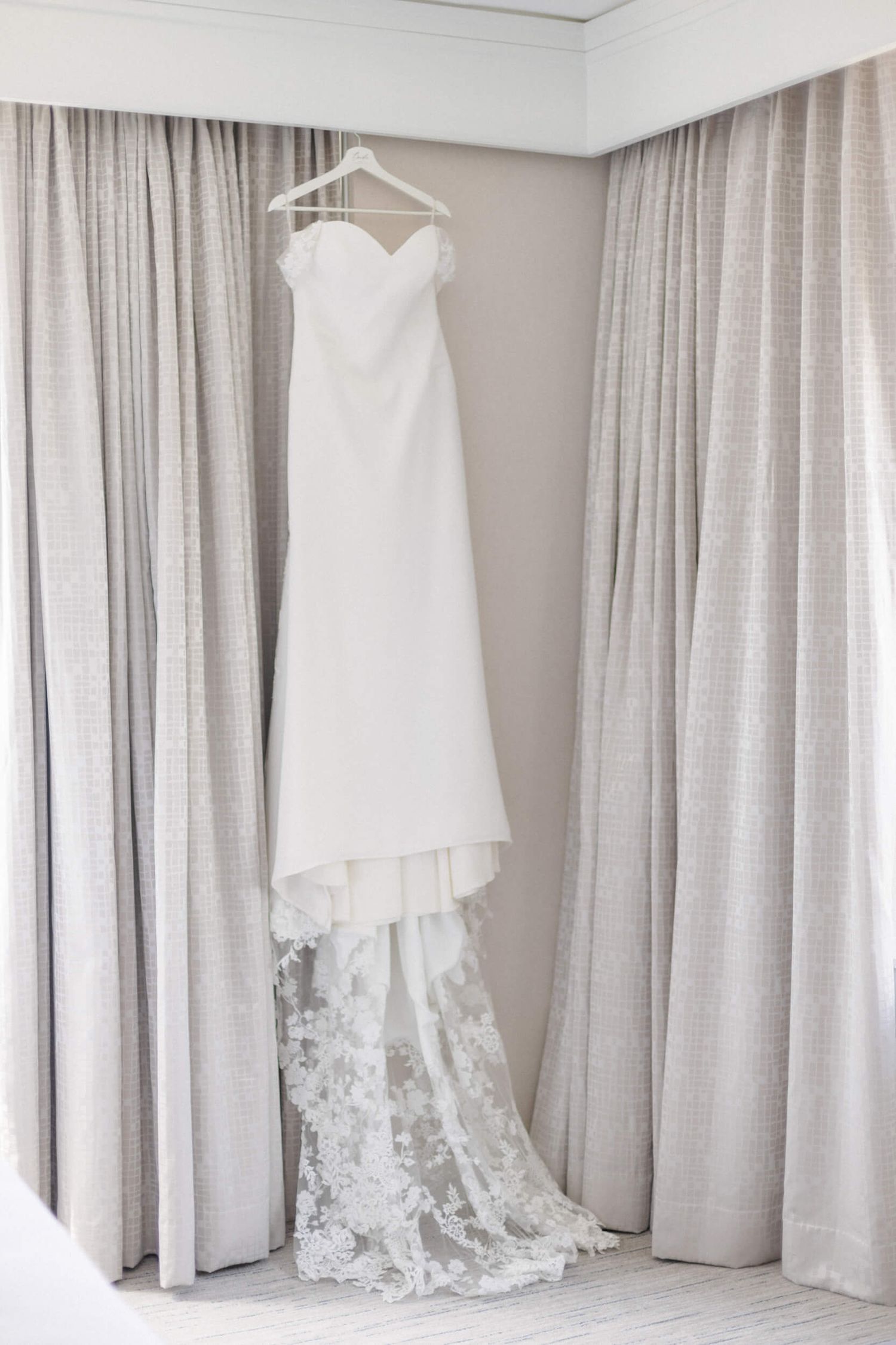 Elegant white wedding dress hanging on display with lace details and flowing train.