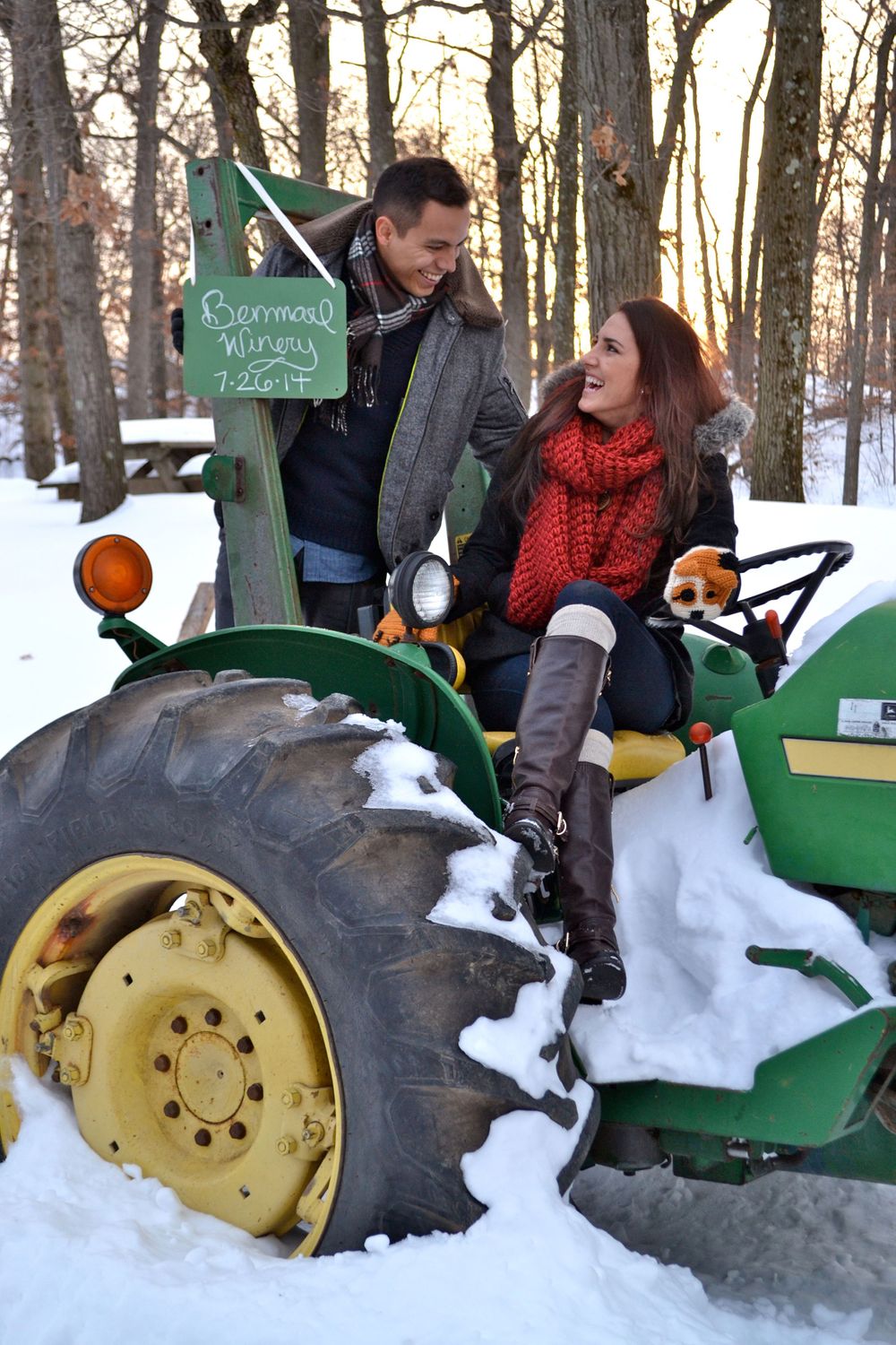 Couple sitting on a vintage green tractor covered in snow during winter.