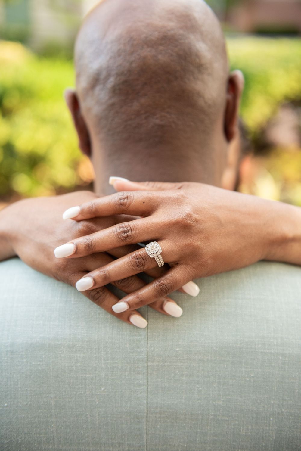 Manicured hands with rings embrace from behind showing wedding jewelry.