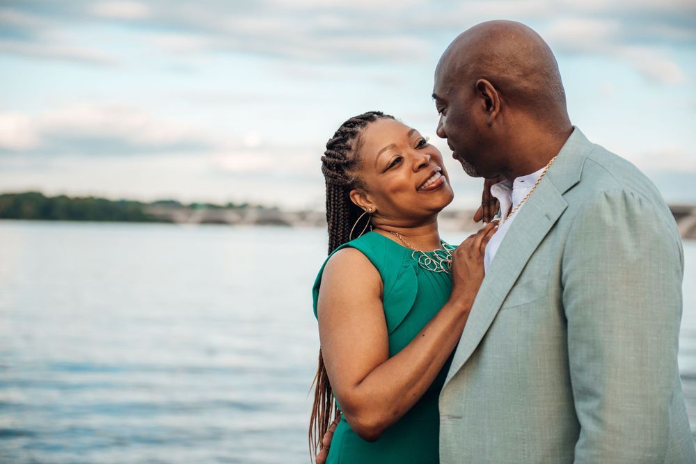 Couple in elegant attire sharing romantic moment by waterfront at sunset.