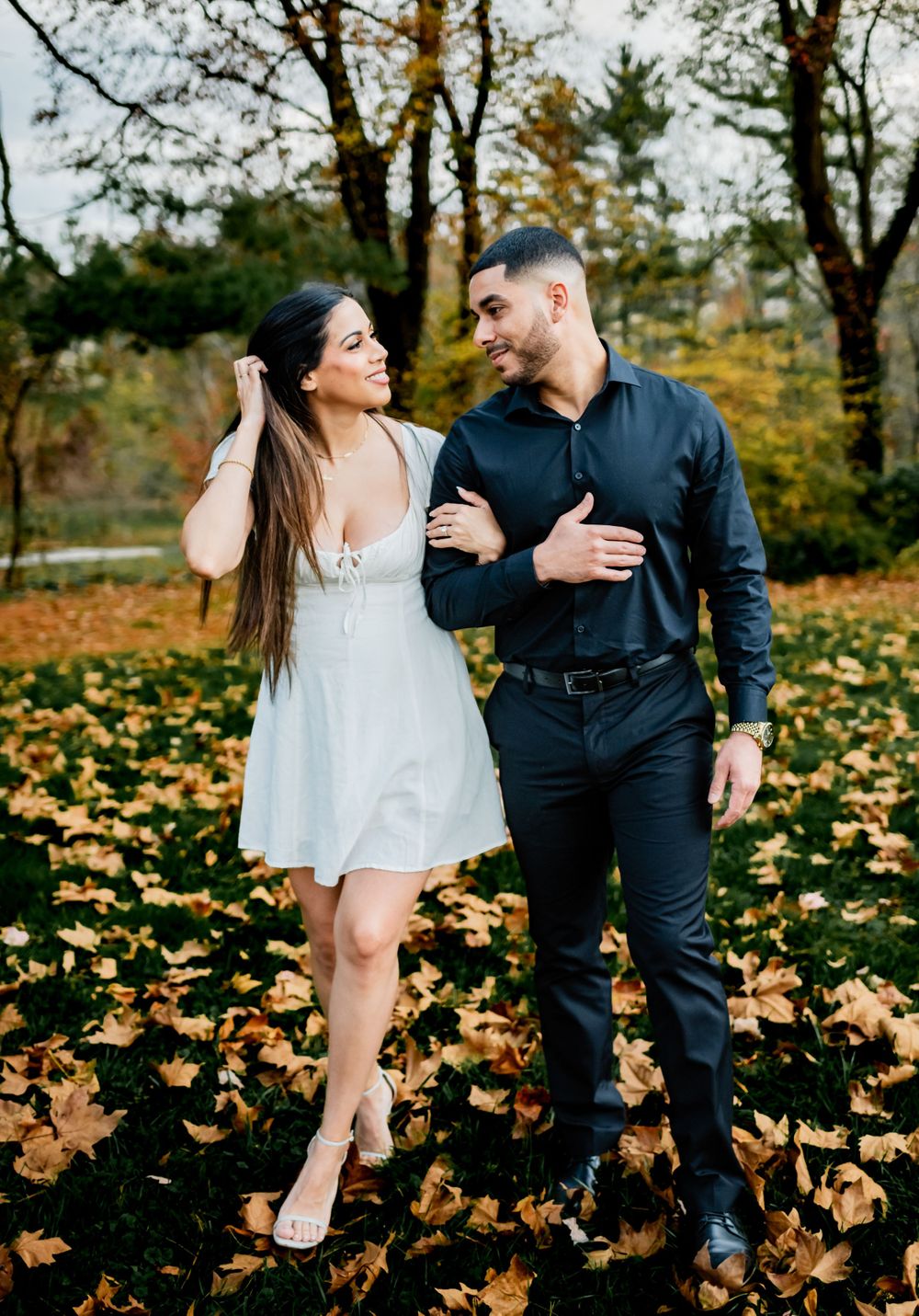 Couple walking together through fallen autumn leaves in coordinated formal attire.