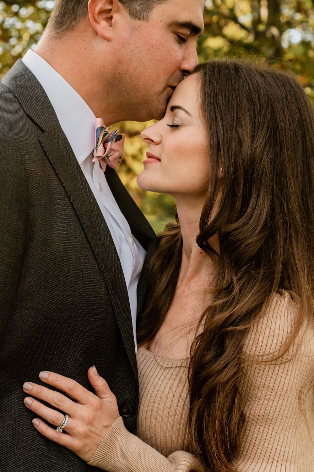 A romantic couple in formal wear sharing an intimate moment outdoors with autumn foliage.