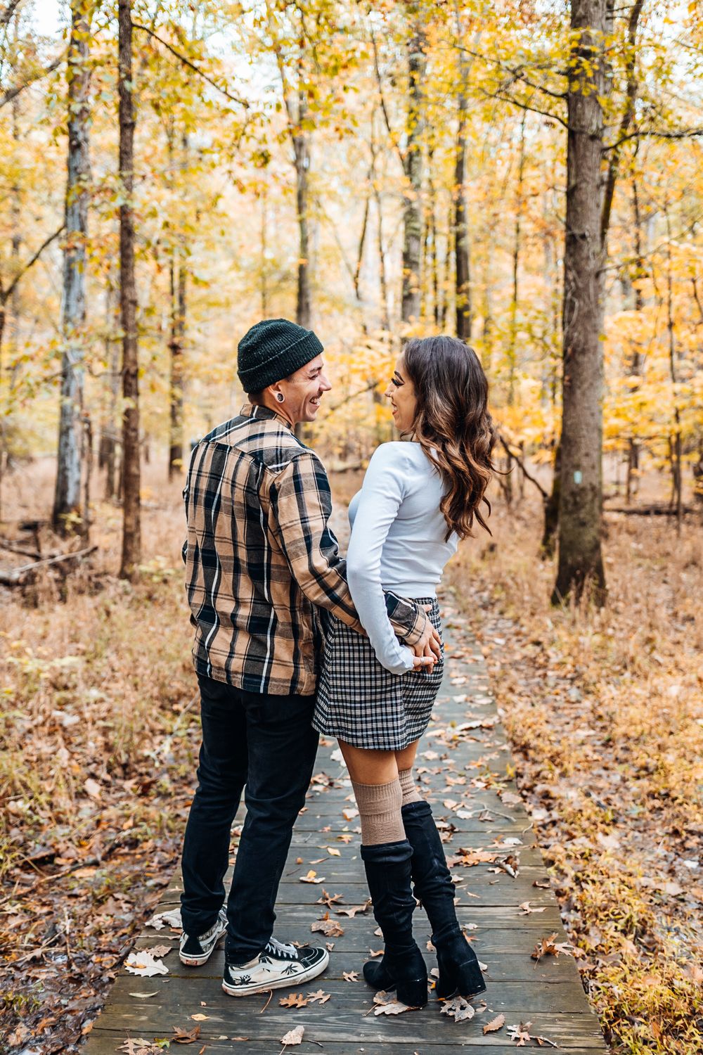 A couple standing on a wooden walkway surrounded by golden fall foliage.