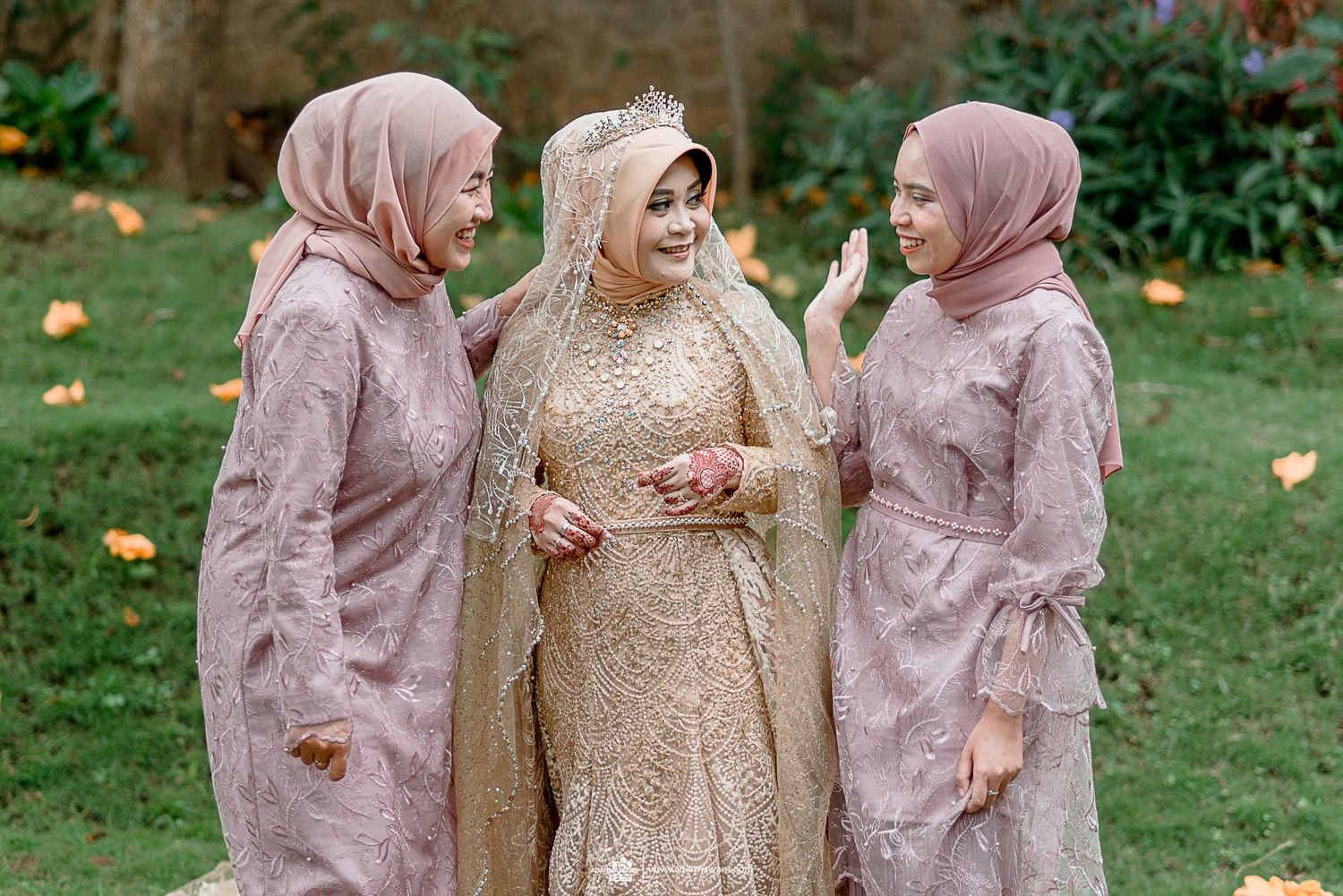 Bridesmaids in matching mauve hijabs surround laughing bride in gold dress outdoors.