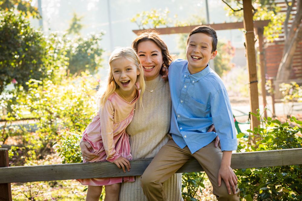 Three people share joyful laughter while sitting together on a wooden fence in golden sunlight.