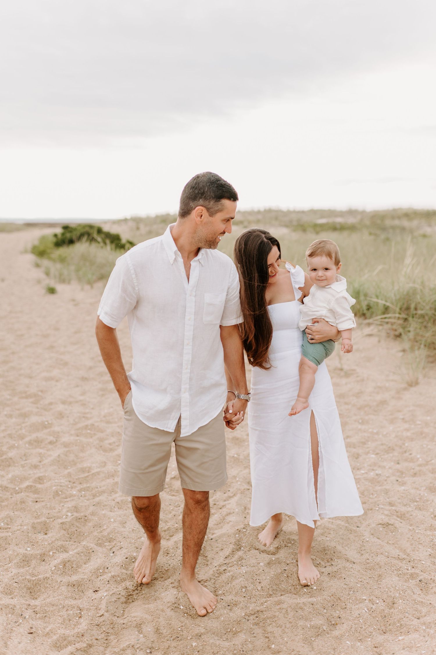 Barefoot family walking together on sandy path during sunset.