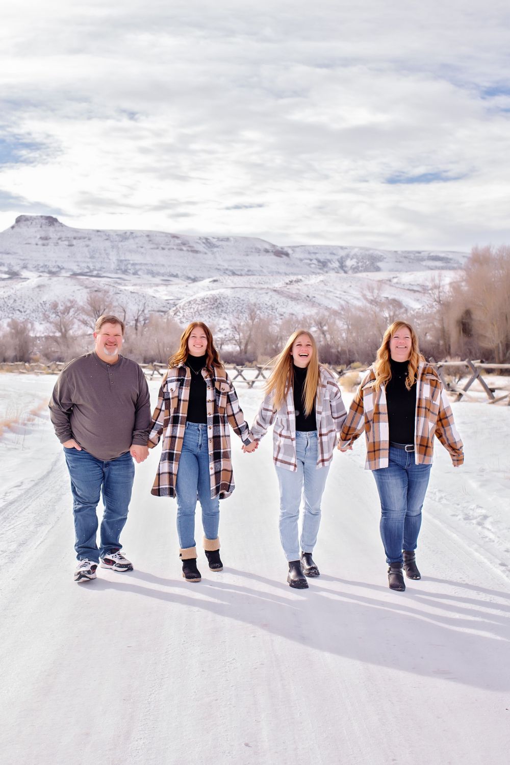 Four people walking together on a snowy path with snow-covered mountains in the background.