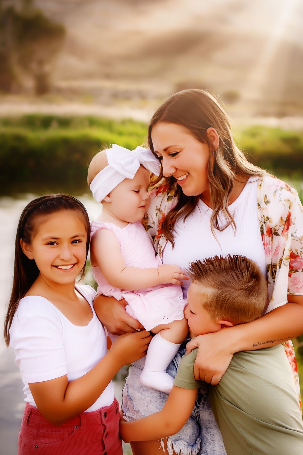 Family enjoying a tender moment together outdoors in warm sunlight near a pond.