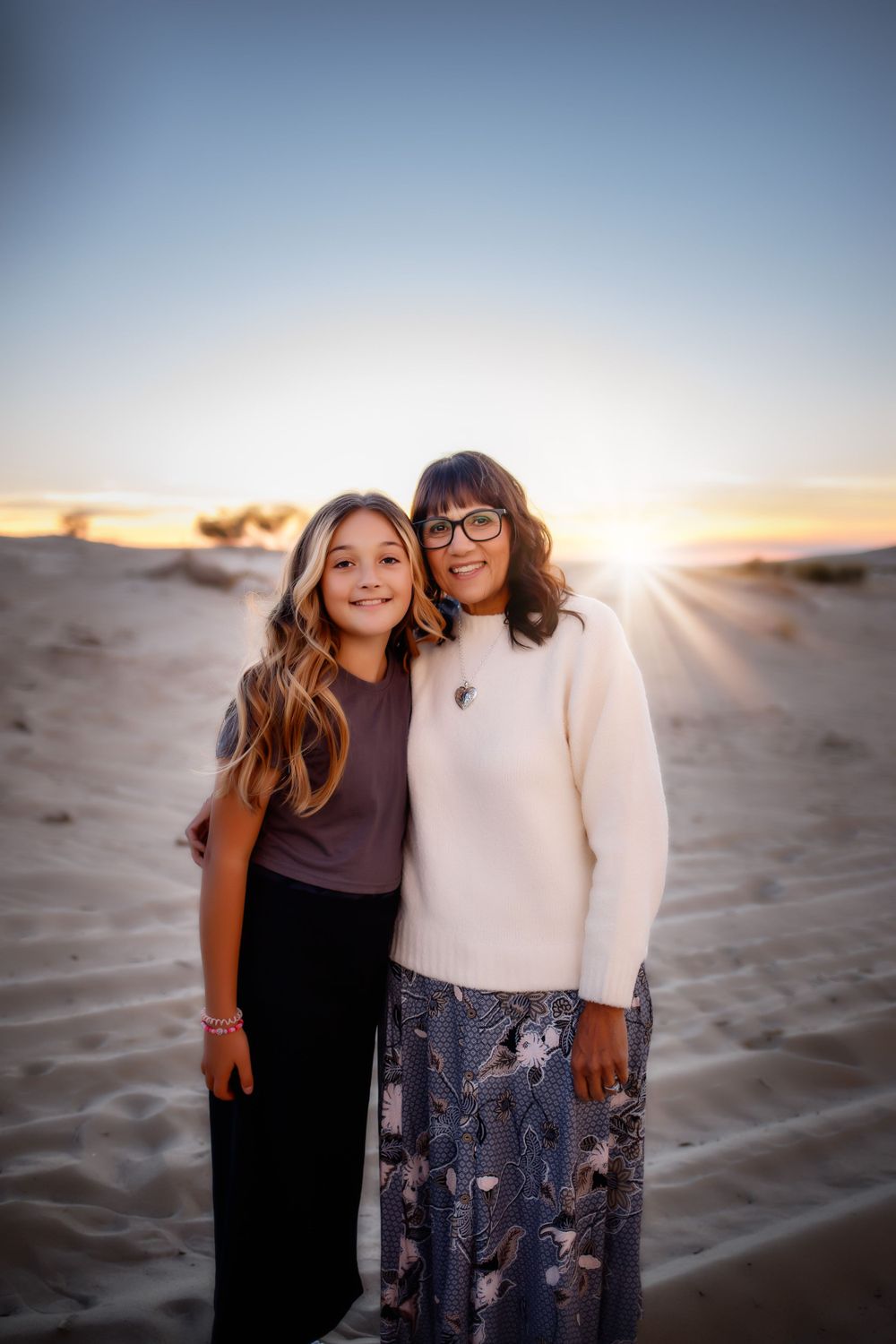 Two people pose together on sandy dunes during golden hour sunset.