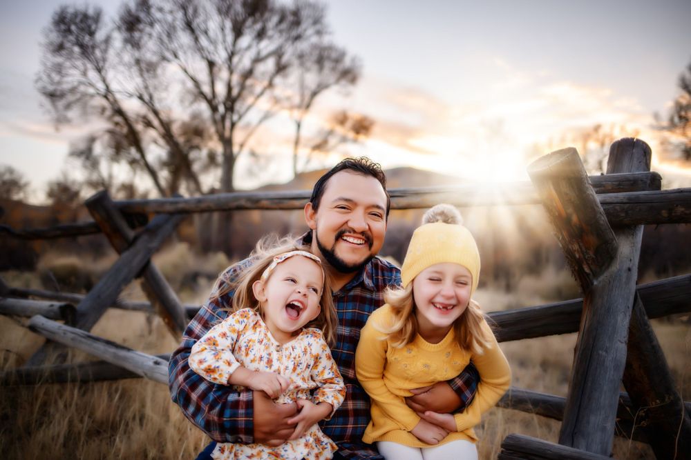 A joyful moment captured at sunset with three people laughing by a wooden fence.