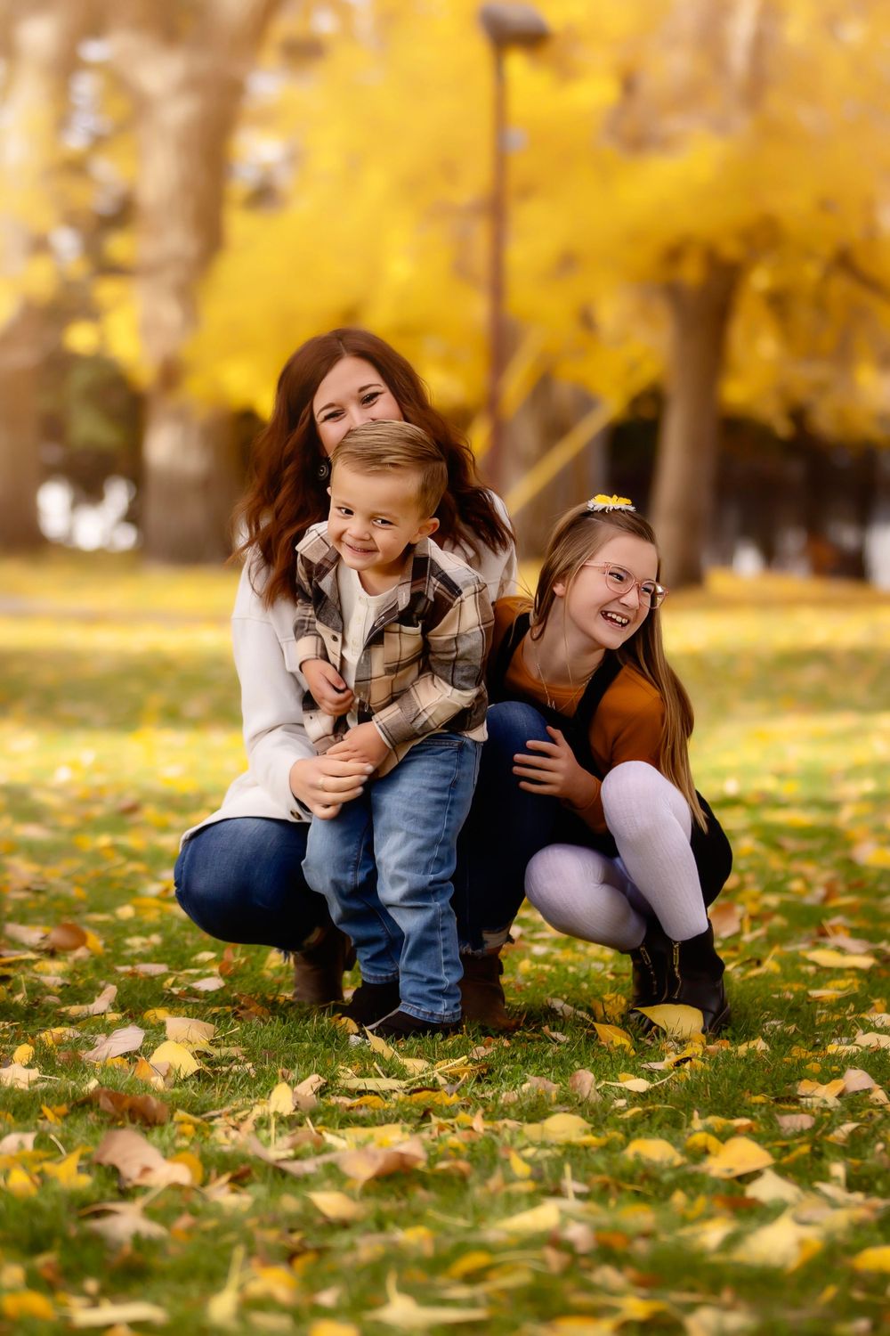 A fall family portrait with golden leaves covering the ground in a park setting.