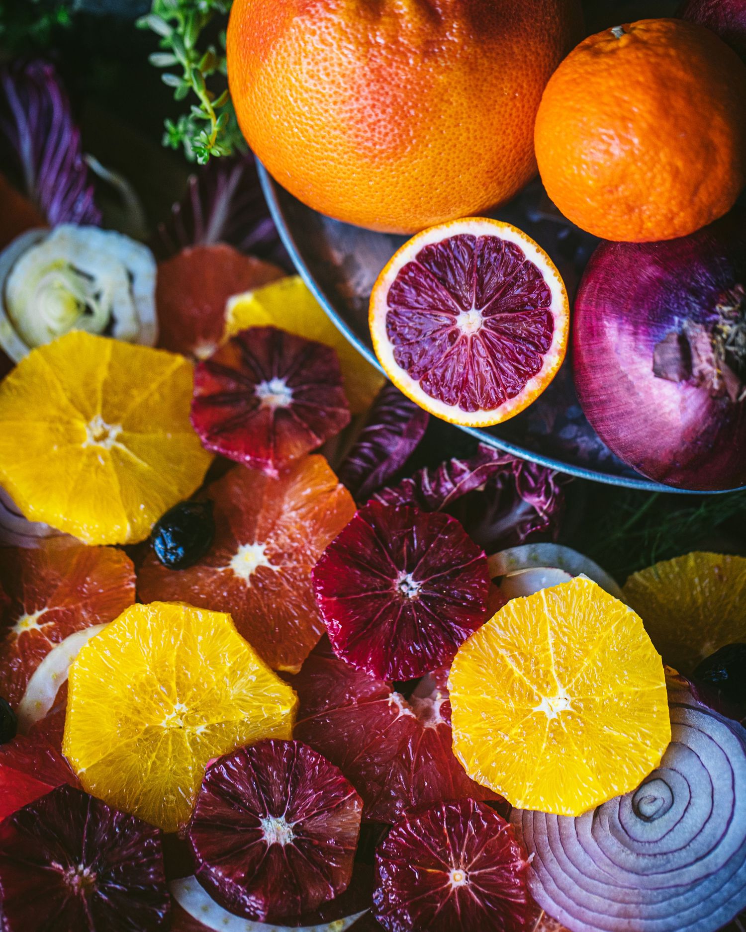 Colorful assortment of sliced blood oranges, navel oranges, and red onions on a rustic surface.