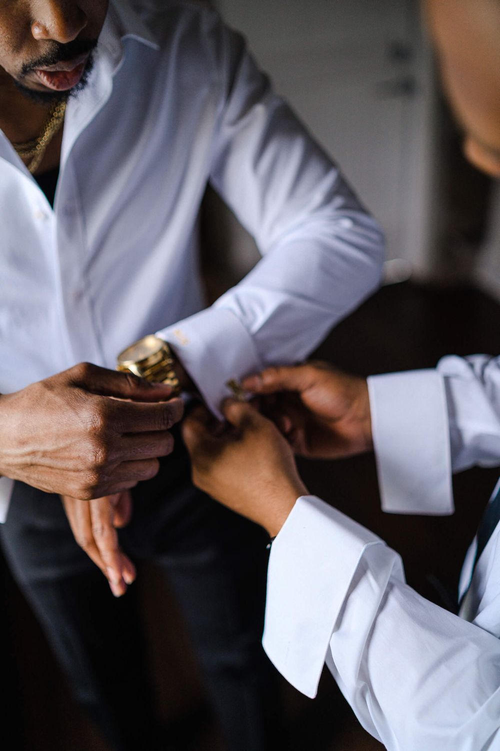 Two people adjust formal attire accessories and cufflinks while getting ready.