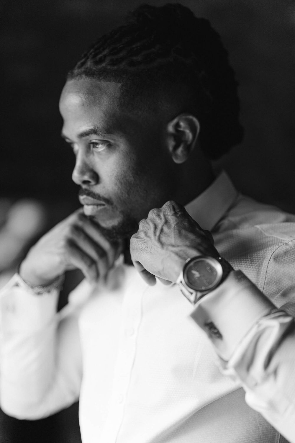 A person in a white shirt wearing a watch gazes contemplatively to the side in black and white.