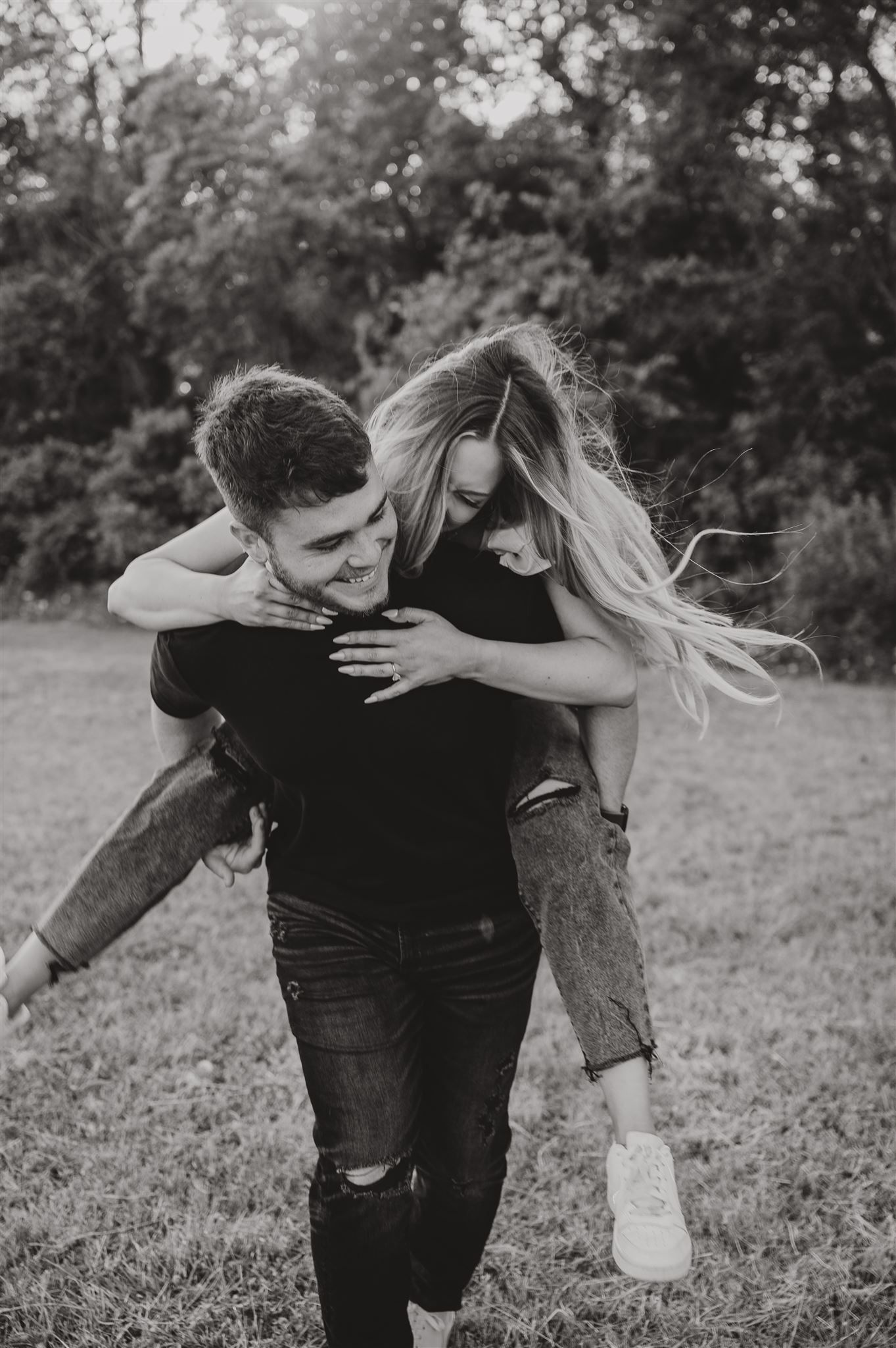 Black and white photo of couple sharing a playful piggyback ride outdoors.